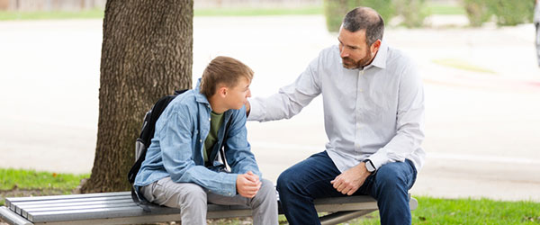 dad sitting on a bench talking with teen son